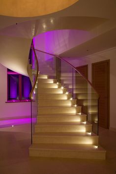 the stairs are lit up with purple lights in this modern home foyer area, which also features a curved staircase