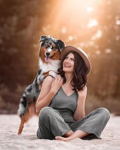 a woman sitting in the sand with her dog