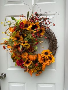 a wreath with sunflowers and other flowers hanging on the front door to welcome guests