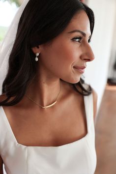 a woman in a white dress wearing a gold necklace and earrings with a veil over her head