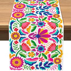 an image of a colorful table runner on a wooden table with flowers and leaves painted on it