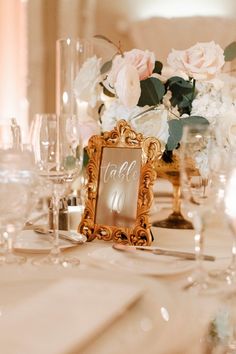 the table is set with white and pink flowers, silverware, and an ornate gold frame