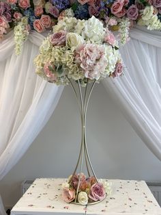 a white table topped with a vase filled with pink and white flowers next to a window