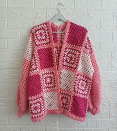 a pink and white crocheted sweater hanging on a wall