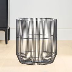 a black wire basket sitting on top of a wooden floor next to a white wall