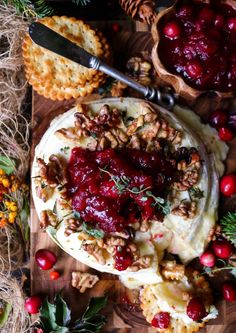 cheese covered with cranberry sauce and nuts on a cutting board next to other food