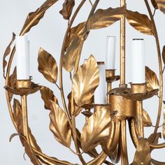 a golden chandelier with three candles in the center and leaves around it, against a white background