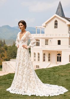 a woman standing in front of a white house wearing a wedding dress with long sleeves