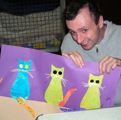 a man is holding up some art work that looks like cats in purple and green