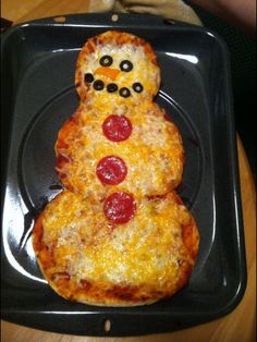 a pizza shaped like a snowman sitting on top of a black plate with pepperoni