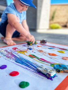 a little boy playing with some toys on the floor in front of a table that has cars painted on it