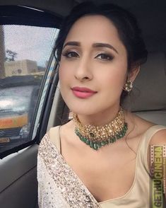 a woman sitting in the back seat of a car wearing a gold and green necklace