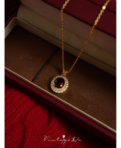 an open box with a necklace in it on top of a red cloth covered table