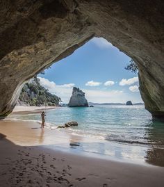 a person is standing in the water under an arch at the beach with footprints on the sand