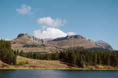 the mountains are covered with trees and clouds in the distance, as seen from a lake