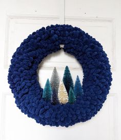 a blue wreath with trees on it hanging from the side of a white door,