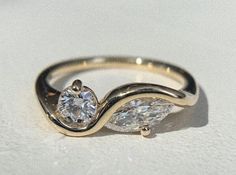 a gold ring with two pear shaped diamonds on it's side, sitting on a white surface