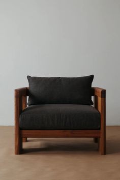 a black chair sitting on top of a wooden floor next to a white wall with a brown pillow