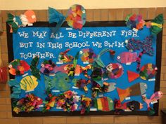 a bulletin board with fish on it in front of a brick wall that says we may all be different fish but in this school we swim together