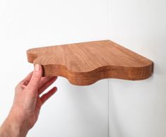 a hand holding a wooden shelf over a white wall