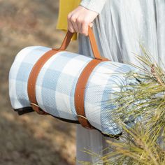 a woman carrying a blue and white plaid bag with brown straps on the handle,