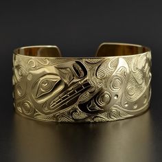 This cuff is hand-engraved and measures 1" wide by 6" long and was designed by First Nations artist Kelvin Thompson. This will fit a wrist between 6 1/4" and 6 1/2" in circumference. Custom lengths can be made on request. This piece is made to order and is titled 'Pod of Whales'.Whales usually signify longevity and strong community bonds due to their tendency to travel in close multi-family pods. In artworks, Orcas can be identified by a large, snub-nosed head; elongated nostrils; a wide, toothy Symbolic Formal Jewelry With Etched Details, Formal Symbolic Etched Jewelry, Unique Yellow Gold Cuff Bracelet For Formal Occasions, Carved Symbolic Yellow Gold Jewelry, Yellow Gold Symbolic Carved Jewelry, Symbolic Carved Jewelry For Formal Occasions, Luxury Engraved Cuff Bracelet For Anniversary, Formal Engraved Bangle Cuff Bracelet, Unique Gold Bangle With Polished Finish