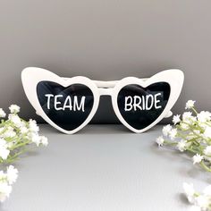 two heart shaped sunglasses with the words team bride written on them next to some flowers