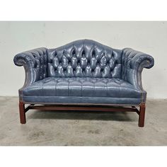 a blue leather couch sitting on top of a cement floor next to a white wall