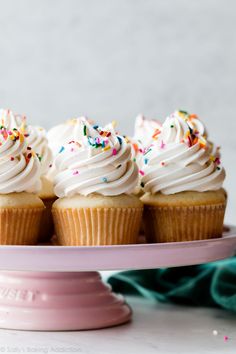 cupcakes with white frosting and sprinkles on a pink plate