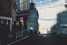 a person standing on the side of a road next to a tall building with a blue sign