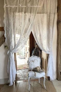 a white chair sitting in front of a window covered in curtains and laces on the walls