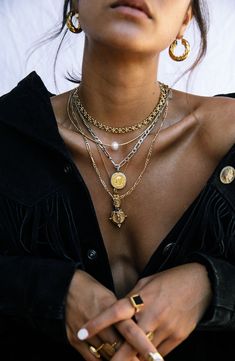 a close up of a person wearing gold jewelry and holding her hands in their pockets