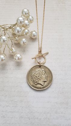 a gold necklace with a coin and pearls on the chain, next to some flowers