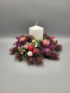 a white candle surrounded by christmas decorations and greenery on a grey background with copy space