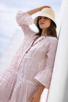 a woman in a pink dress and hat leaning against a wall with her hand on her head