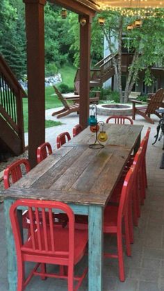 an outdoor dining area with red and blue chairs, wooden table and lights hanging from the ceiling