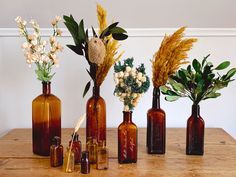 five brown bottles with flowers and plants in them on a wooden table next to each other