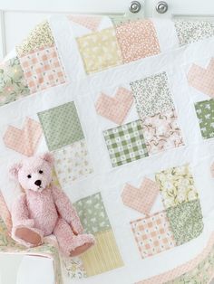 a pink teddy bear sitting on top of a bed next to a patchwork quilt