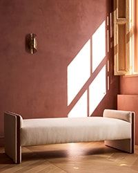 a white bench sitting in the middle of a room next to a window with sunlight streaming through it