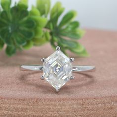 a white diamond ring sitting on top of a wooden table next to a green plant