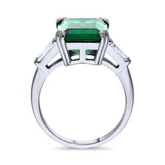 an emerald and diamond ring with three stone accents on the sides, set in white gold