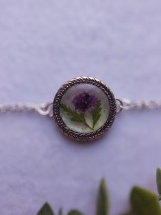 a necklace with a flower in the center on a white table next to some leaves