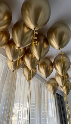 gold balloons are hanging from the ceiling in front of a window with sheer drapes