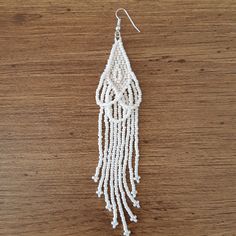 a pair of white beaded earrings hanging from a hook on a wooden table top