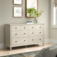 a white dresser sitting in a bedroom next to a window with pictures on the wall