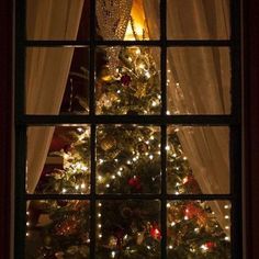 a lit christmas tree is seen through a window