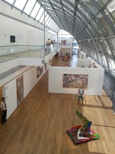 the inside of an art museum with people looking at artwork on display and paintings on the walls