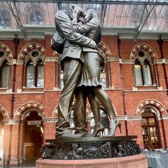 there is a statue of two people hugging each other in front of a large building