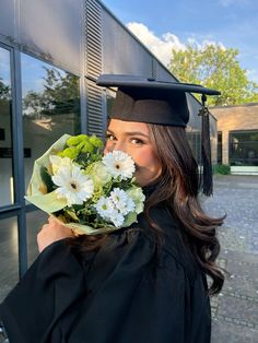 a woman wearing a graduation cap and gown holding flowers