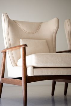 an upholstered chair with wooden legs and arm rests against a white wall in the background